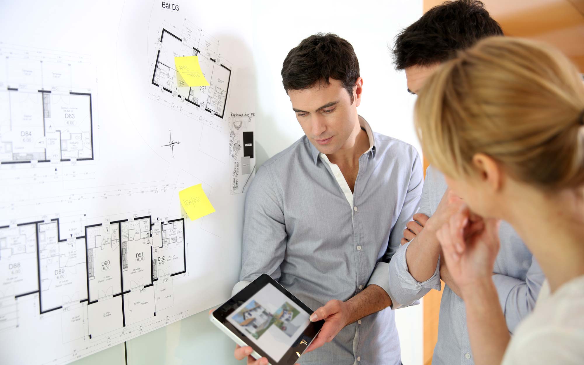 man showing ipad to another couple with blueprints